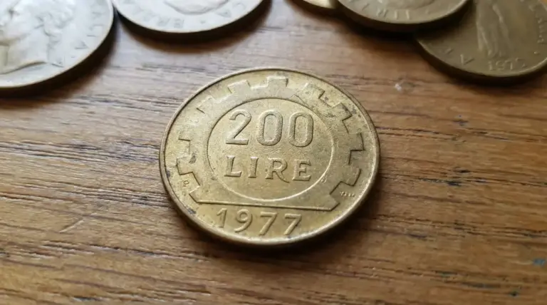 Moneta da 200 lire del 1977 su tavolo in legno, affiancata da altre monete italiane