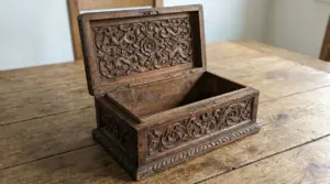 Antico portagioie in legno intagliato con coperchio aperto su tavolo in legno