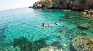 Persona che fa snorkeling in acque cristalline vicino alla costa rocciosa italiana