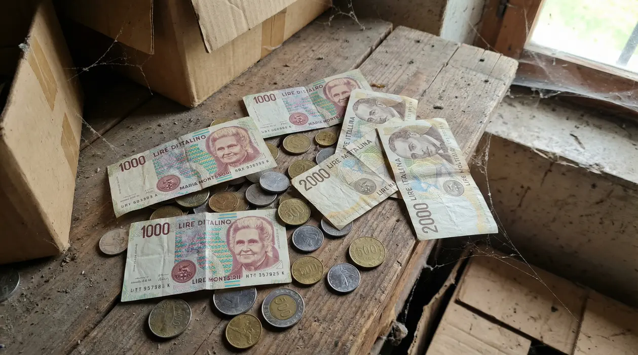 Vecchie banconote e monete italiane in lire su un tavolo impolverato in soffitta